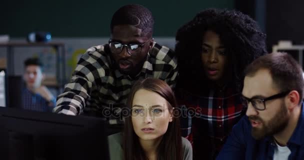 Young multi-ethnical team of office workers having a discussion about a startup project late at night. Group of friendly proffesionals looking at the computer in the urban office space. — Stock Video