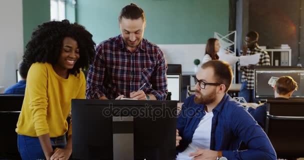 As raças mistas jovens sorriram colegas de trabalho que falam e discutem o projeto de negócio no espaço de escritório moderno. Equipe amigável em um ambiente acolhedor . — Vídeo de Stock