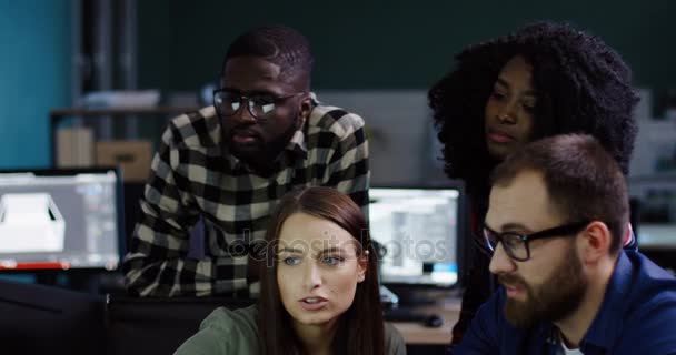 Unga manliga och kvinnliga arbetare diskuterar ett affärsprojekt vid datorn i natt. Vänliga blandade raser team i urban office. — Stockvideo