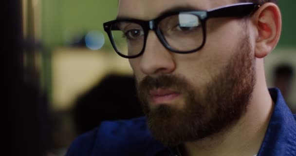 Κοντινό πλάνο του προσώπου όμορφος νεαρός άνδρας Καυκάσιος γυαλιά που εργάζονται αργά στον υπολογιστή. Η θολή φόντο. Εσωτερικούς χώρους. Πορτρέτο — Αρχείο Βίντεο