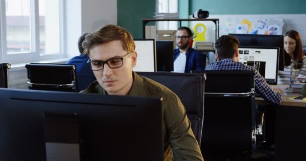 Retrato de un guapo joven rubio caucásico trabajando en la oficina en la computadora. La oficina moderna con los trabajadores de fondo . — Vídeos de Stock