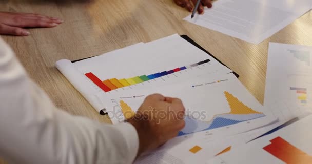 Vista superior de manos de razas mixtas trabajando y tratando con documentos en papel, gráficos, informes financieros, diagramas y gráficos en la mesa de madera blanca. Lluvia de ideas del equipo empresarial — Vídeos de Stock