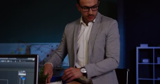 Joven hombre guapo con gafas empacando sus cosas en la oficina tarde en la noche porque está despedido. Trabajador de oficina perdió su trabajo. Adentro. — Vídeo de stock