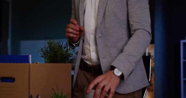 Großaufnahme eines jungen kaukasischen männlichen Büroangestellten mit Brille, der spät in der Nacht im Büro seine Sachen in die Schachtel packt, weil er gefeuert wird. Mann verlor seinen Job. Innenräume — Stockvideo