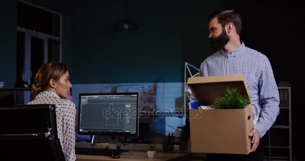 Attractive sad office worker with a beard carrying a box with his stuff walking out from the office room late at night because he is fired. Male employee lost his job. Indoors — Stock Video