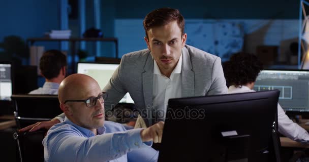 Joven trabajador de negocios caucásico recibiendo instrucciones de su jefe sobre el proyecto empresarial de startup. Oficina urbana con trabajadores tarde en la noche sobre fondo borroso. En interiores — Vídeos de Stock