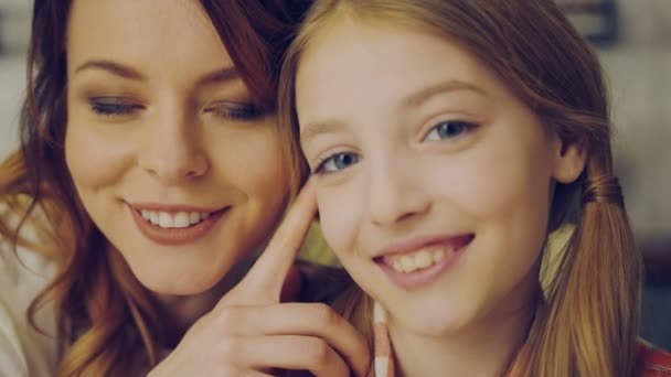 Close up of the beautiful mother and her teen daughter standing closely cheek to cheek and smiling in the camera. Portrait. Indoor — Stock Video