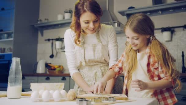 kleines hübsches Mädchen hilft ihrer Mutter beim Plätzchenbacken, Tochter formt eine Tochter und zeigt es ihrer Mutter in der Küche. Innenräume