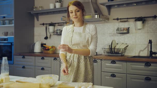 Portrait de la jolie femme dans le tablier et avec une farine sur le visage souriant à la caméra dans la cuisine tout en cuisinant et en croisant les mains. À l'intérieur — Video