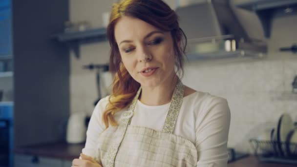 Primer plano de la hermosa mujer en el delantal y con una harina en la cara posando en la cocina mientras cocina y cruza las manos. Retrato. En interiores — Vídeo de stock