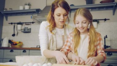 Öğretim ve mutfak masasının üzerinde hafta sonu bir daugh için çerezleri yapmak genç sarışın kızı için gösterilen güzel anne. Kapalı