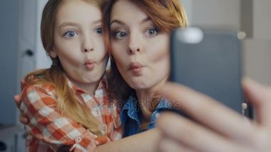 Bir genç kızı sarılma ve komik selfies yapması sırasında belgili tanımlık smartphone üzerinde yapma gülümseyen anne kapatın. Portre. İçinde