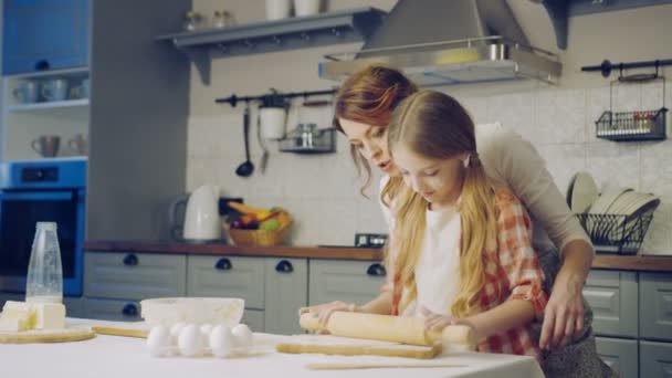 Schöne Frau und ihre kleine Tochter, die abends eine Tochter für die Plätzchen auf dem Küchentisch macht. drinnen — Stockvideo