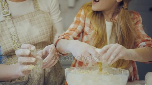 Close up das mães e filhas mãos quebrando um ovo para a tigela de vidro com uma daugh dentro. Retrato filmado na cozinha enquanto cozinha . — Vídeo de Stock