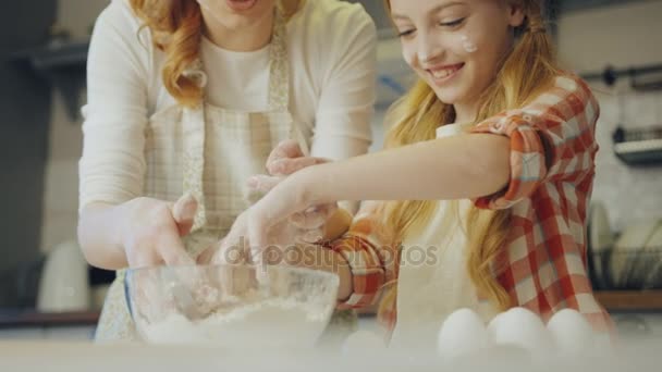 Boldog fiatal anya tini szőke lánya mutatja hogyan dagasztás egy daugh, egy tálba, amíg teszi az élelmiszerek a konyhában. Közelről. Beltéri — Stock videók