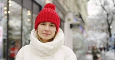 kapatmak yukarıya-in orta yaşlı tarafından bakarım ve samimi bir gülümseme ile kamera başına dönme sıcak kış ceket ve kırmızı şapkalı güzel sarışın kadın. Açık havada. Portre