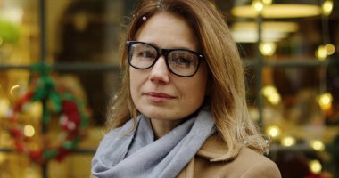 Orta yaşlı kadının kafasını kameraya dönüm ve kar yağıyor iken gülümseyen bardaklarda kapatın. Noel pencere durumda arka plan üzerine dekore edilmiştir. Portre. Dışarıda