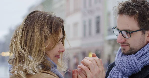 Close up do lindo casal de meia-idade de pé perto, olhando um para o outro suavemente e homem que aquece as mãos das mulheres no dia nevado na cidade. Tiro de retrato. Ao ar livre . — Fotografia de Stock