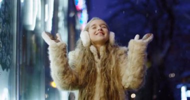 Mutlu güzel kız uzun sarı saçlı kış akşamları Dükkanı vitrin yağıyor iken çevresinde elleriyle dönmektedir. Açık.