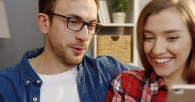 Sarışın genç gülümseyen kadın bir şey yakışıklı erkeğini onlar birbirine yakın oturan ve güzel odaya gülüyor için onun smartphone ekranında gösterilen kapatın. Portre. İçinde