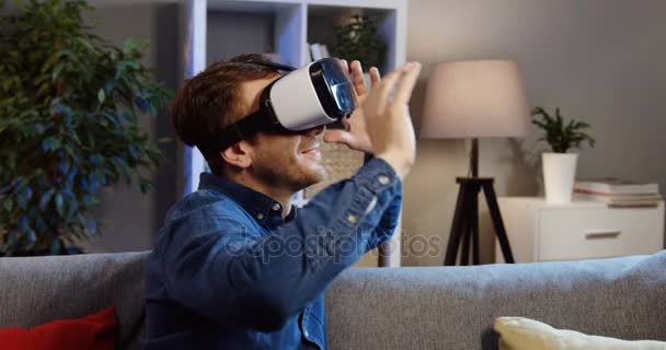 Närbild av den unga manen i Vr-glasögon sitter i soffan i vardagsrummet och med Vr-headset. Kvällstid. Porträtt skott. Inomhus — Stockvideo