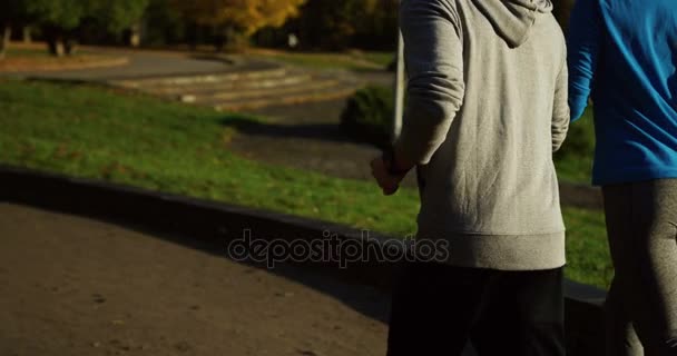 Sorrindo casal desportivo de corredores correndo no parque de outono. Fechar os pés a correr. Traseira. Ao ar livre — Vídeo de Stock