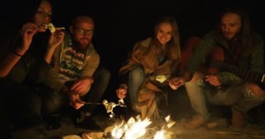 Dört erkek ve kadın arkadaş hipsters marshmellows şenlik üzerinde pişirme ve onları gece zamanında yemek. Açık havada