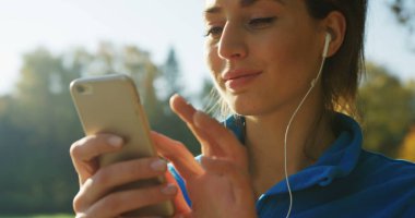 Parkta rahatlatıcı Kulaklığımda çekici kadının seçme ve çalıştırmadan önce telefonda müzik dinlemek süre yakın çekim. Güneşli havalarda. Dışarıda. Portre vurdu