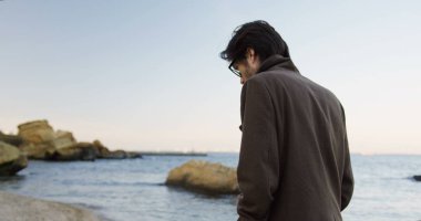 Den kayalık sahil gezinme ve sabah düşünme yakışıklı depresif adam arkasında görüntüleyin. Açık havada