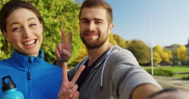 Kamerada poz ve zafer işareti ve pazı güneşli sabah gösterilen kadın ve erkek gülümseyen genç kapatın. Park içinde erken sonbahar. Portre, açık. POV