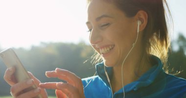 Parkta rahatlatıcı Kulaklığımda çekici kadının seçme ve çalıştırmadan önce telefonda müzik dinlemek süre yakın çekim. Güneşli havalarda. Dışarıda. Portre vurdu