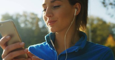 Parkta rahatlatıcı Kulaklığımda çekici kadının seçme ve çalıştırmadan önce telefonda müzik dinlemek süre yakın çekim. Güneşli havalarda. Dışarıda. Portre vurdu