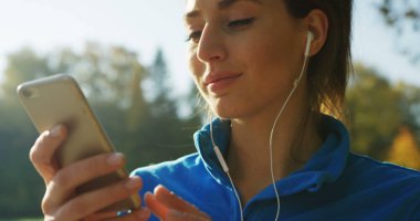 Parkta rahatlatıcı Kulaklığımda çekici kadının seçme ve çalıştırmadan önce telefonda müzik dinlemek süre yakın çekim. Güneşli havalarda. Dışarıda. Portre vurdu