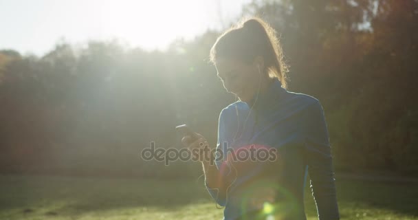 Bastante deportivo mujer jogger silueta caminando en el parque y grabando en el teléfono. El clima soleado en la mañana de otoño agradable. Afuera. — Vídeos de Stock