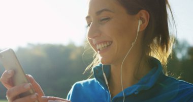Parkta rahatlatıcı Kulaklığımda çekici kadının seçme ve çalıştırmadan önce telefonda müzik dinlemek süre yakın çekim. Güneşli havalarda. Dışarıda. Portre vurdu