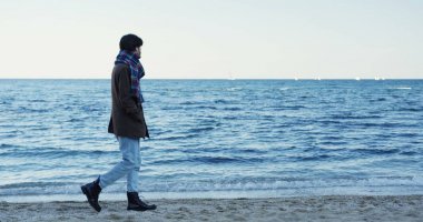 Sealine arasında sahilde yürüyen yakışıklı adam. Melankolik Hava bulutlu gökyüzü ile. Deniz horizont. Dışarıda.