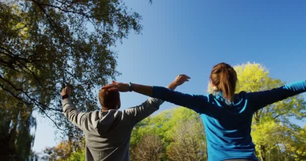 Sportieve paar oefenen en rekken in het zonnige park in de vroege ochtend. Yoga buiten. Achteraanzicht. — Stockvideo