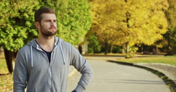 Portrait of young attractive man jogger looking on the side and then turning to the camera and laughing in the park in early autumn. Outdoors. Sunny day — Stock Video