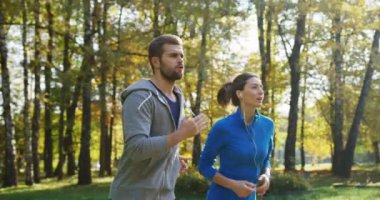 Ağır çekim güneşli parkta koşu genç sportif çift taraftan. Erken sonbahar güzel havalarda. Dışarıda