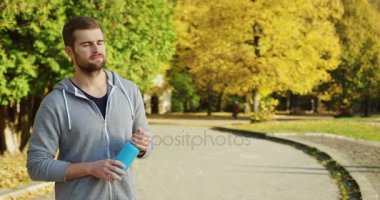 Mavi şişe tarafında ve sonra güneşli parkta kamerada içine erken seyir ile beyaz sportif yakışıklı düşmek genç portresi. Dışarıda