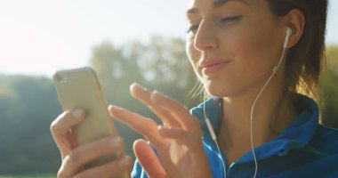 Parkta rahatlatıcı Kulaklığımda çekici kadının seçme ve çalıştırmadan önce telefonda müzik dinlemek süre yakın çekim. Güneşli havalarda. Dışarıda. Portre vurdu