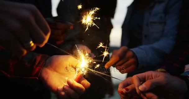 Feche-se das mãos de corridas mistas jovens que mantêm faíscas e iluminam-se com um isqueiro em um tempo de crepúsculo. Ao ar livre — Vídeo de Stock