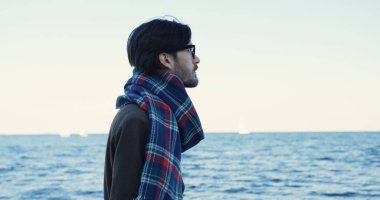 Çekici bir adam sahilde yürüyüş bardaklarda tarafındaki kapatın. Melankolik Hava bulutlu gökyüzü ile. Deniz horizont. Dışarıda.