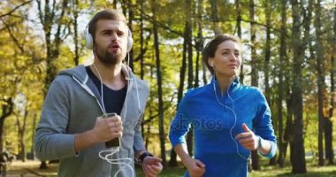 Kadar yakın ve yavaş hareket güneşli parkta koşu kulaklık sportif genç çiftin. Erken sonbahar güzel havalarda. Dışarıda