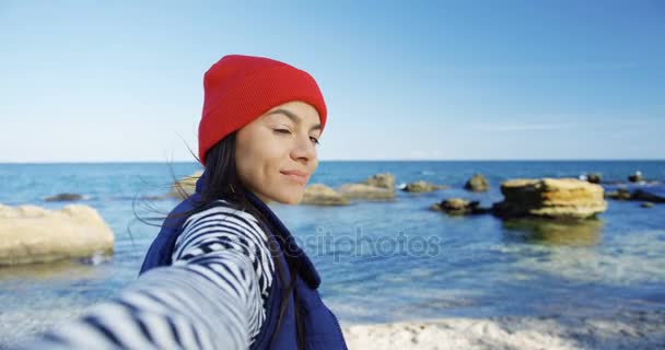 Giovane bella donna che cammina sulla riva rocciosa del mare, sorridendo sinceramente nella fotocamera e facendo mi seguono. All'aperto. Tempo soleggiato. Punto di vista. Da vicino. — Video Stock