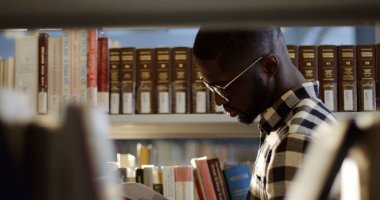 Afrikalı-Amerikalı genç adam ayakta kitaplar arasında ise kitabın sayfaları çevirme bardaklarda tarafındaki portre kütüphanede temizleyelim. Yakın çekim. Açık havada