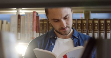 Kitaplar kütüphane rafları arasında bir kitap okuma yakışıklı genç kapatın. Portre vurdu. Kapalı