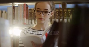 Genç kız öğrenci ile raflar arasında kitap okuma bardaklarda portre çekim kütüphanede kitap. Yakın çekim. Kapalı