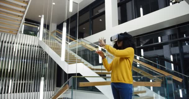 Αφρικανική αμερικανική γυναίκα με σγουρά μαλλιά στέκεται στη μέση το σύγχρονο κτίριο ωραίο και έχοντας μια συσκευή VR, δακτυλογράφηση και δέσει στον αέρα. Εσωτερική — Αρχείο Βίντεο