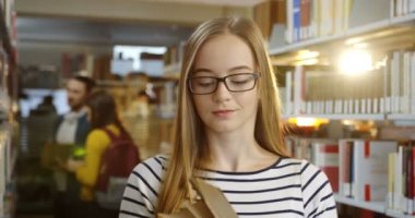 Kütüphanede duran ve açma ve okuma daha bir kitap seçerek gözlüklü sarışın beyaz kadının kapatın. Portre. İçinde